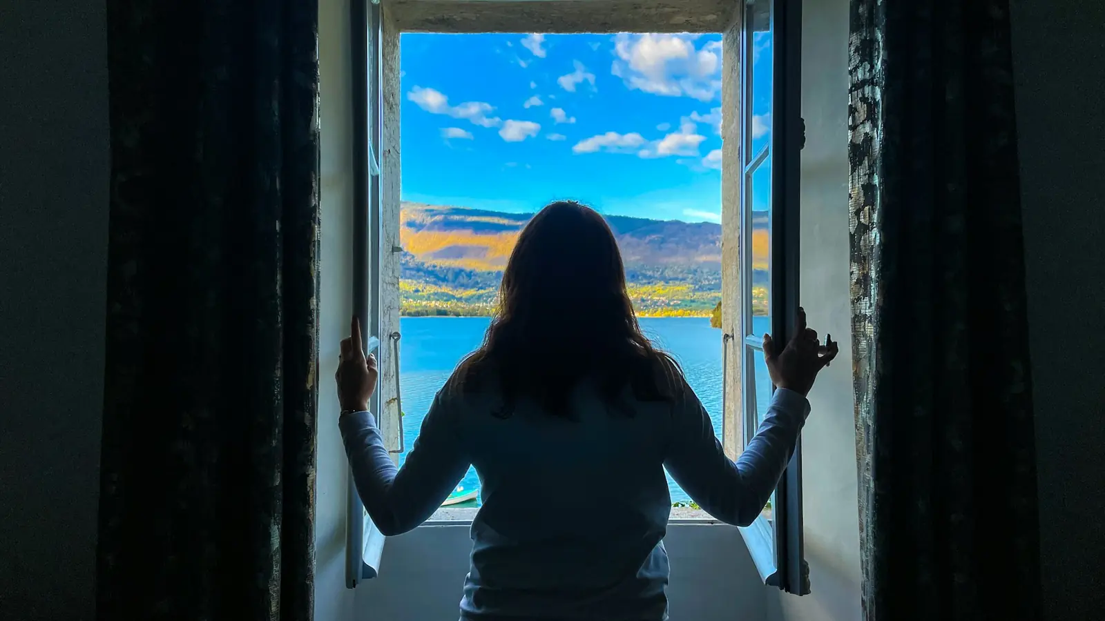 Eine Frau öffnet weit das Fenster zu einem See unter blauem Himmel